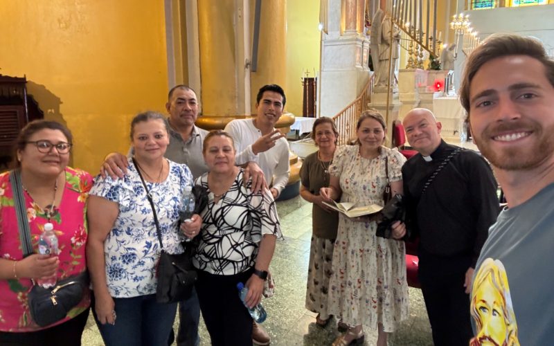 Integrantes de la misión y fieles salvadoreños sonríen juntos dentro de una iglesia, con vitrales al fondo