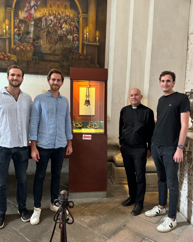Tres integrantes del equipo y un sacerdote junto a la vitrina con la campanita del Santo Hermano Pedro, en su museo de Antigua Guatemala