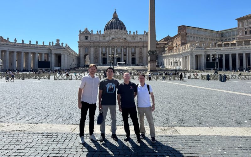 Cuatro integrantes de la misión en la Plaza de San Pedro, con la basílica al fondo
