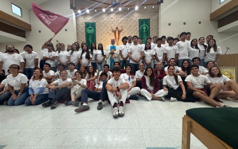 Jóvenes del retiro Bartimeo, con camisetas blancas, junto al sacerdote frente al altar de una iglesia